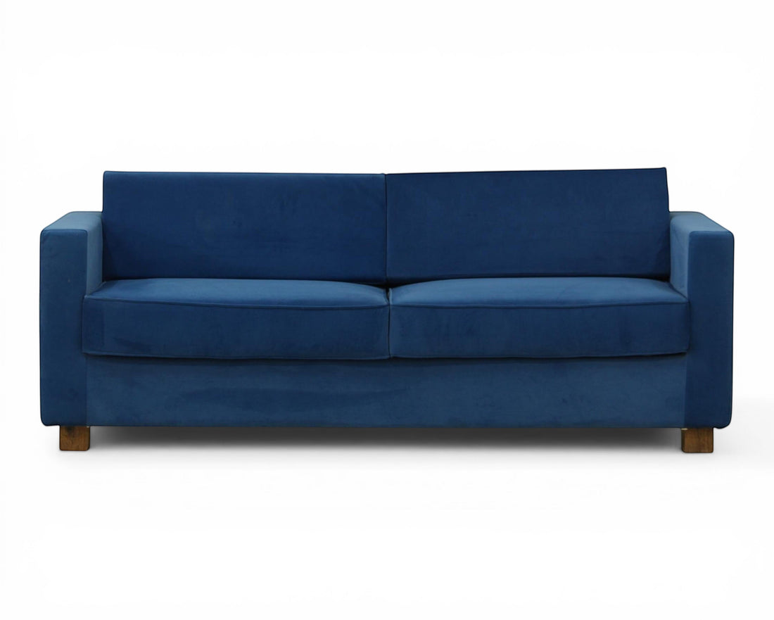 Nakoda Homes blue velvet sofa with clean lines and modern silhouette, plush upholstery, and wooden legs. Includes tan accent pillows.