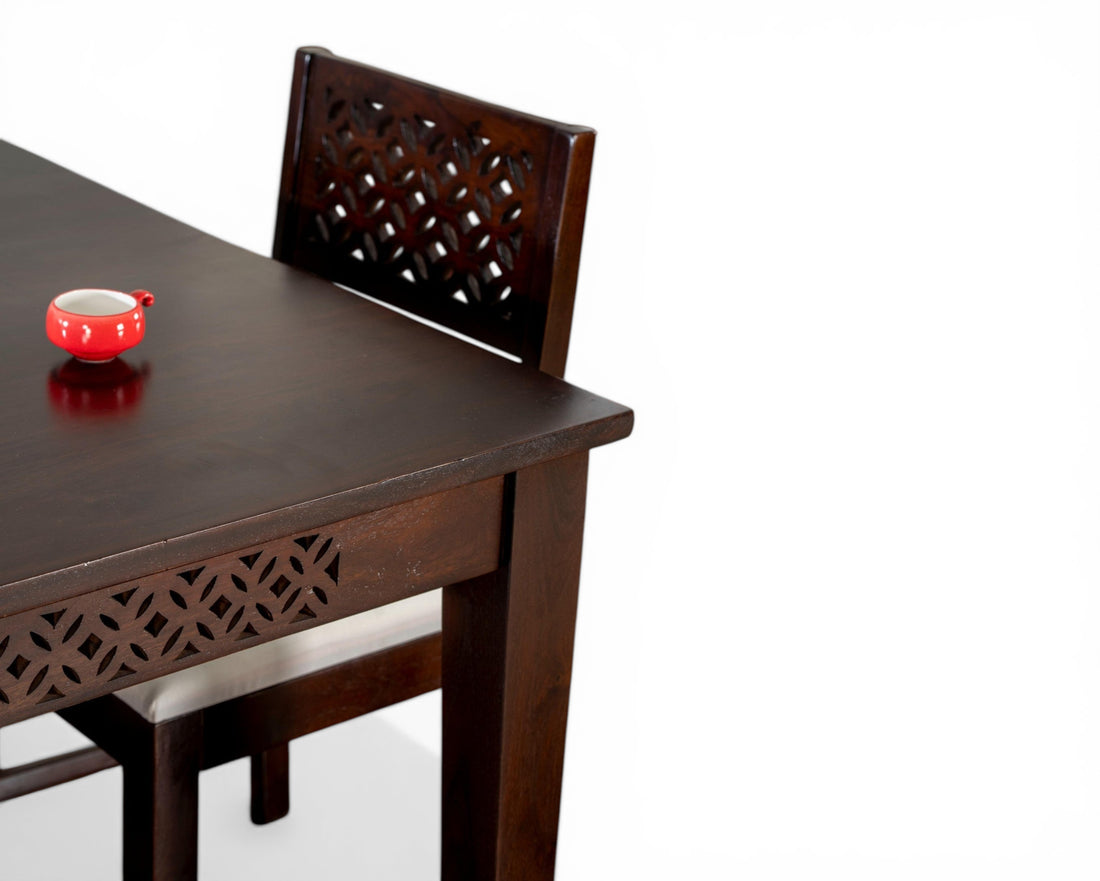Nakoda Homes dark wood dining set with carved detailing and white upholstered chairs. Features geometric carvings on table apron and chair backs.