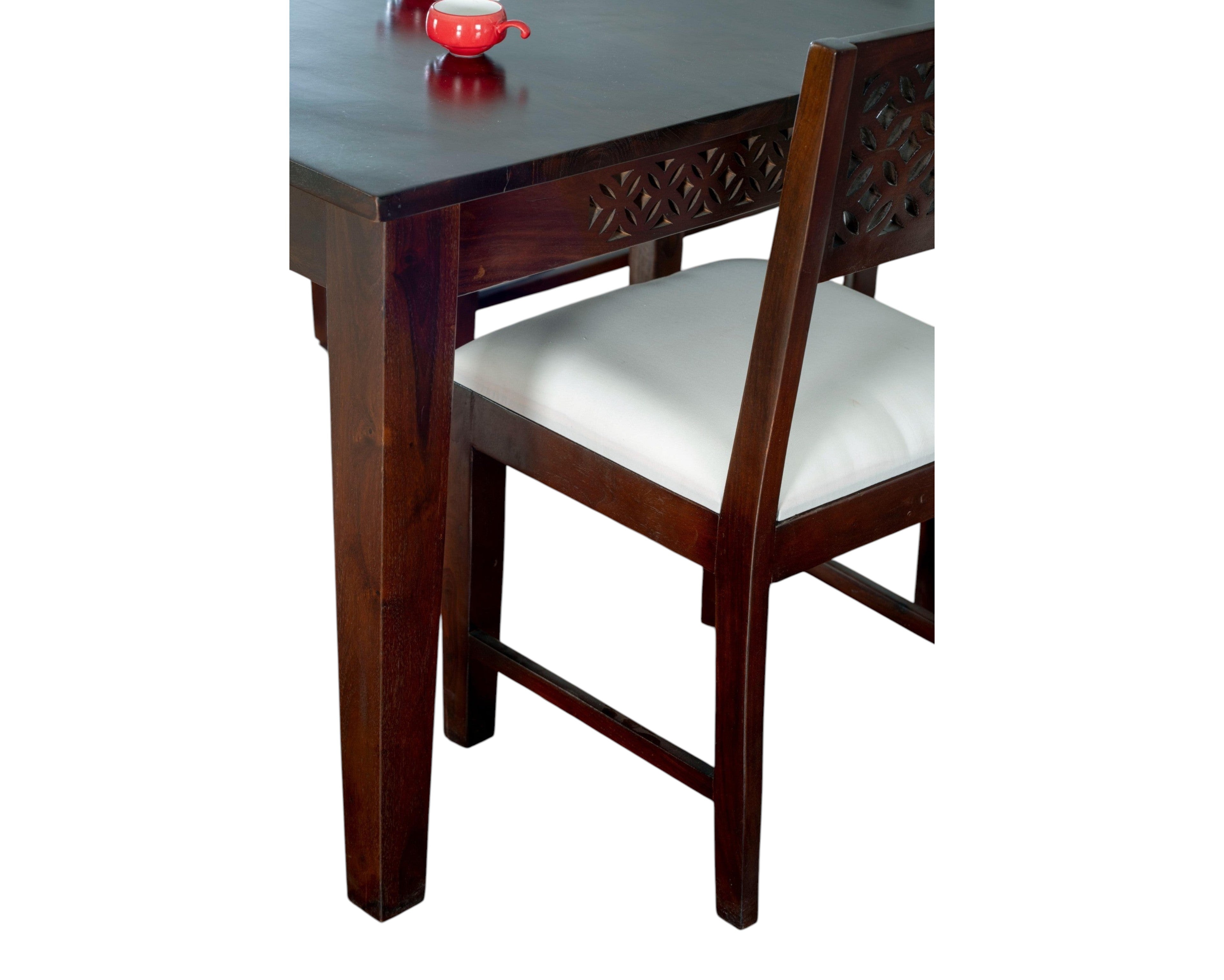 Nakoda Homes dark wood dining set with white upholstered seats and intricate geometric carvings on chair backs and table apron.