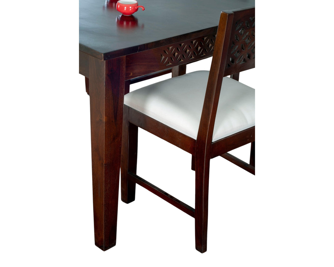 Nakoda Homes dark wood dining set with white upholstered seats and intricate geometric carvings on chair backs and table apron.