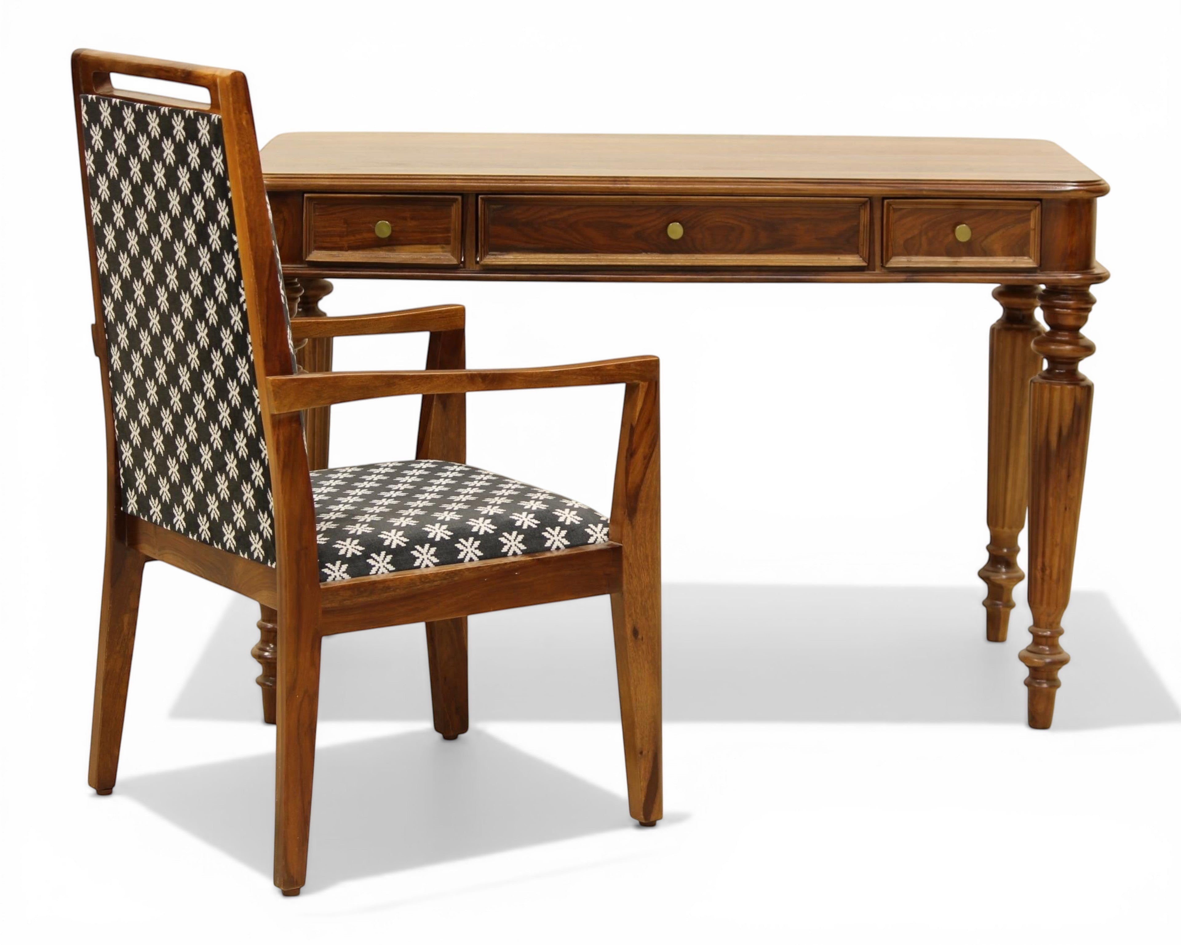 Nakoda Homes dark wood writing desk with three drawers and carved legs, paired with a patterned chair.