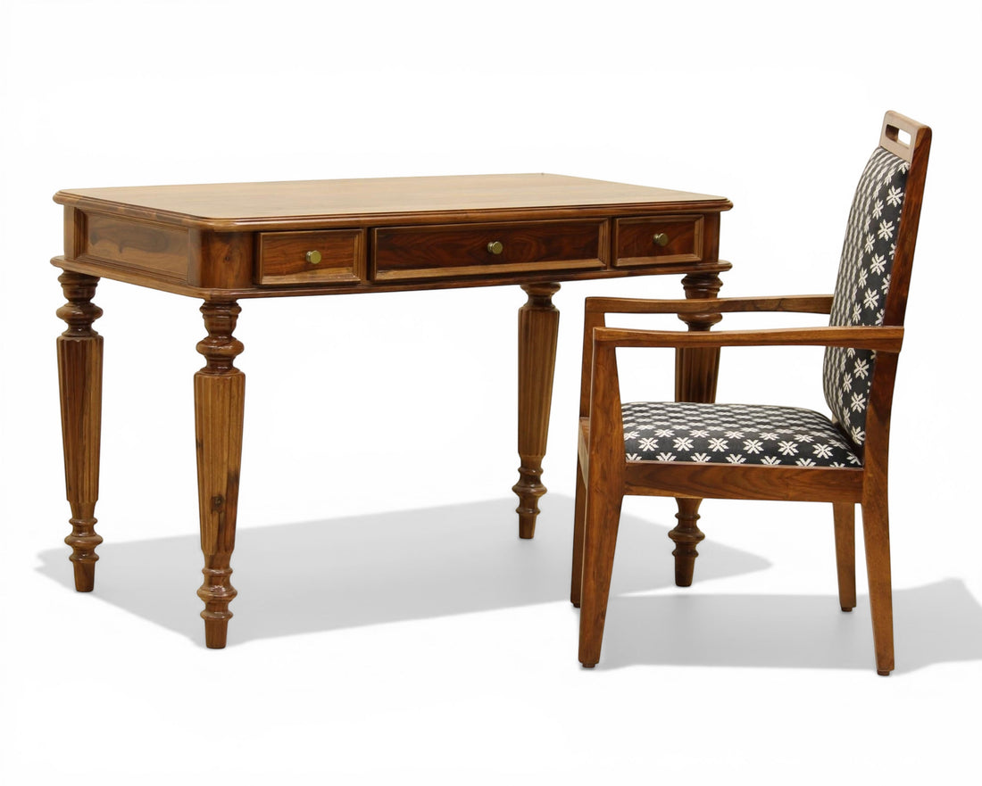 Nakoda Homes dark wood writing desk with three drawers and carved legs, paired with a patterned armchair.
