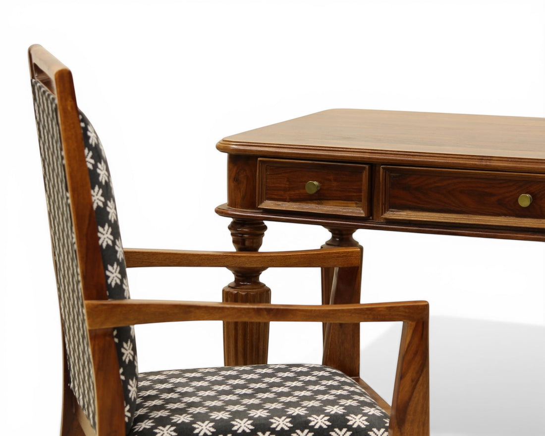Nakoda Homes dark wood writing desk with brass knobs and fluted legs, paired with a patterned armchair.