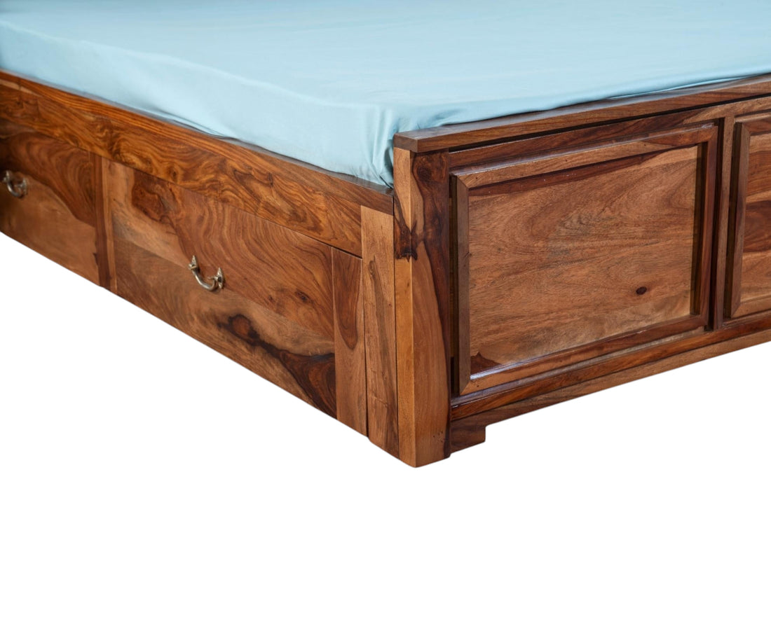 Nakoda Homes Sheesham wood bed frame with carved geometric headboard and storage drawers. Rich wood grain.