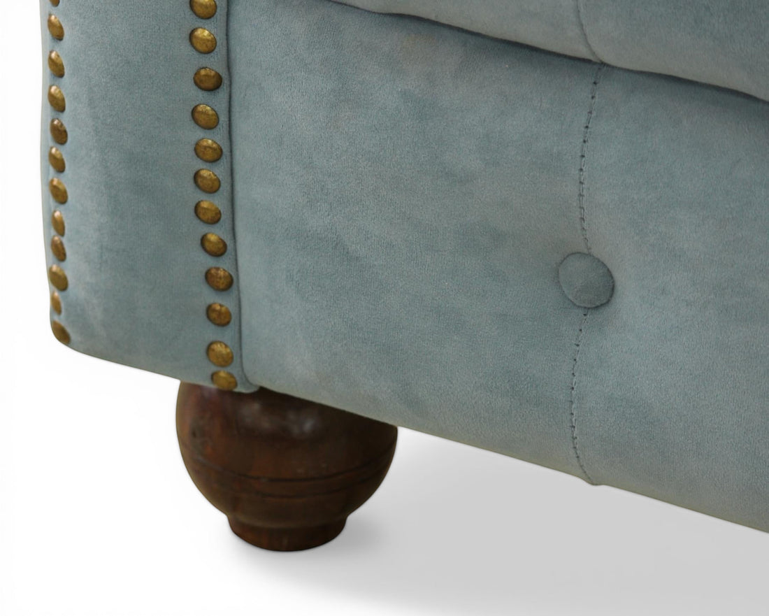 Nakoda Homes sky blue velvet Chesterfield sofa with button-tufting and brass nailhead trim on dark wooden legs.