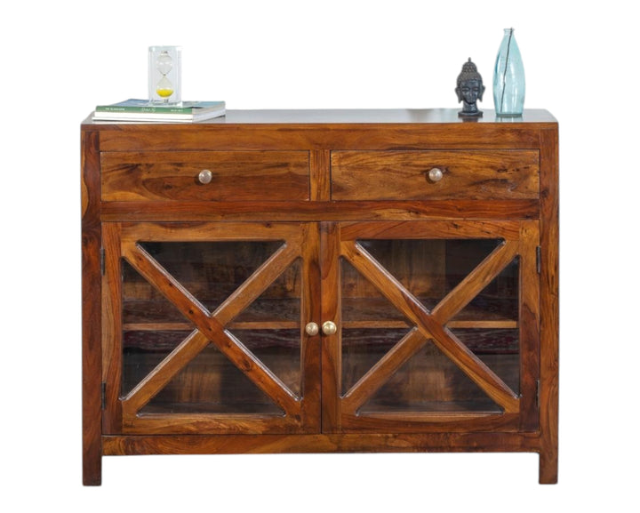 Nakoda Homes solid wood cabinet with glass doors and two drawers. Warm-toned Sheesham wood with natural grain. Rustic criss-cross design on doors.