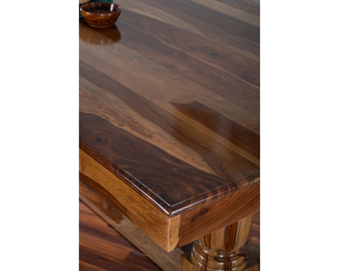 Nakoda Homes solid wood dining table with rich, warm-toned wood grain and pedestal base.