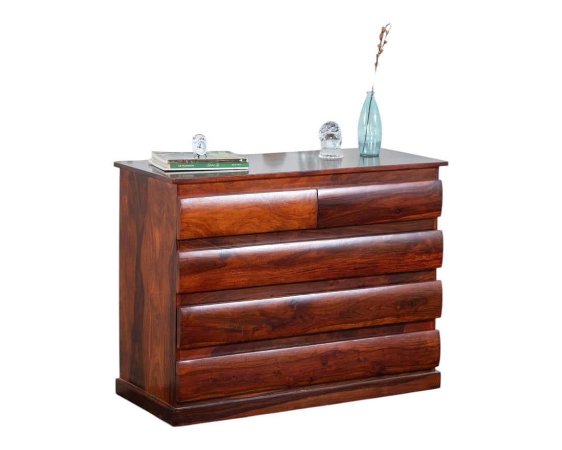 Nakoda Homes solid wood dresser with five drawers featuring curved fronts and natural wood grain. Warm brown finish.
