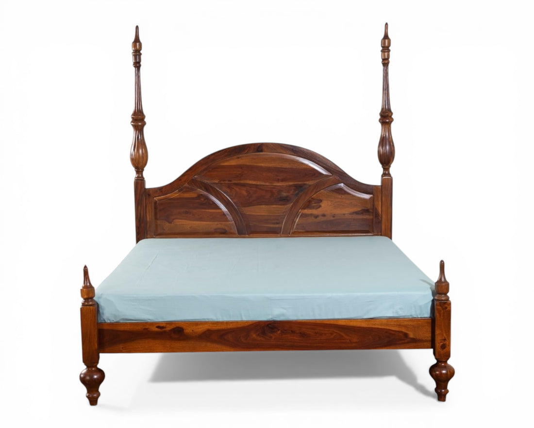 Nakoda Homes solid wood four poster canopy bed with arched headboard and intricate detailing. Warm wood tone.