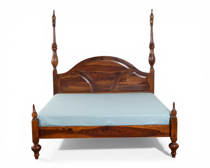 Nakoda Homes solid wood four poster canopy bed with arched headboard and intricate detailing. Warm wood tone.