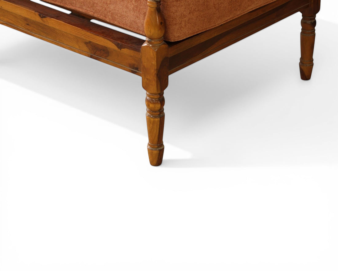 Nakoda Homes rust-colored upholstered loveseat with wooden frame and carved legs, accented with tan pillows.