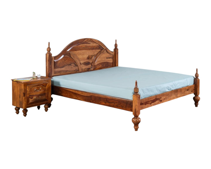 Nakoda Homes solid Sheesham wood bed frame with arched, carved headboard and turned posts. Warm wood tone.